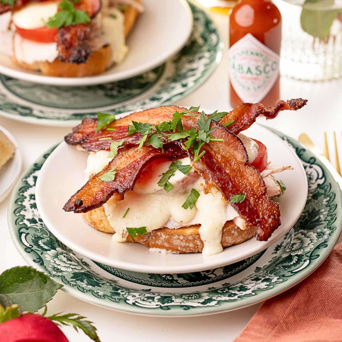 On a white plate sits a Kentucky Hot Brown open-face sandwich topped with bacon and parsley.