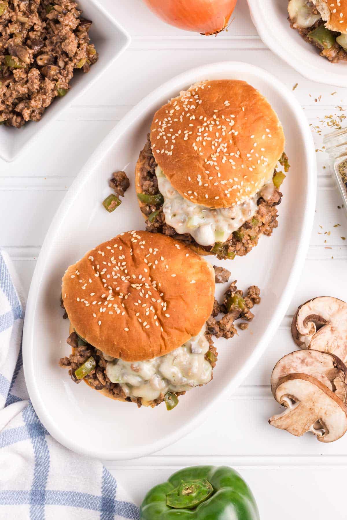 Philly Cheesesteak sloppy joes set on a white platter on a table with all the fixings.