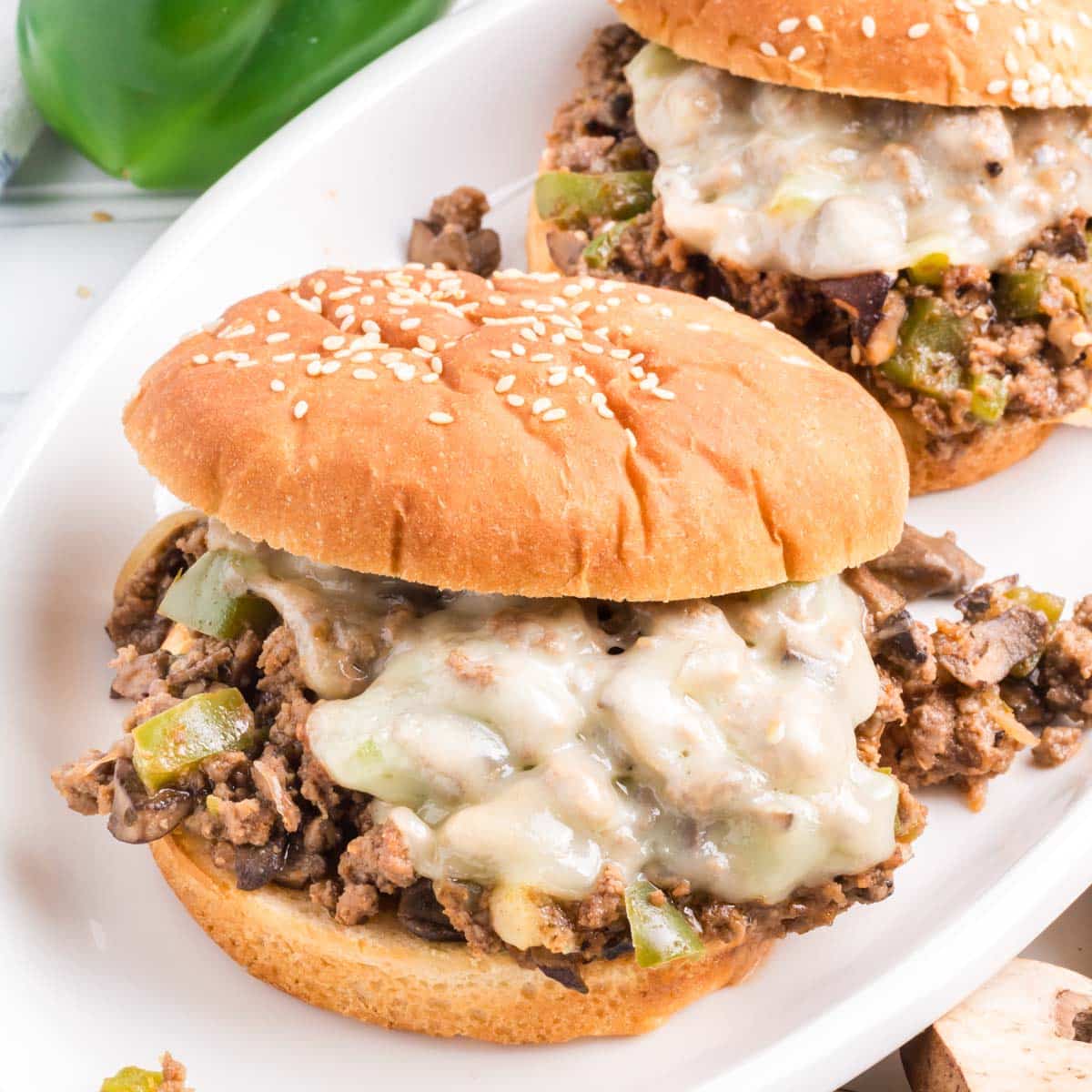 Two Philly Cheesesteak sloppy joes sandwiches on a white serving plate.