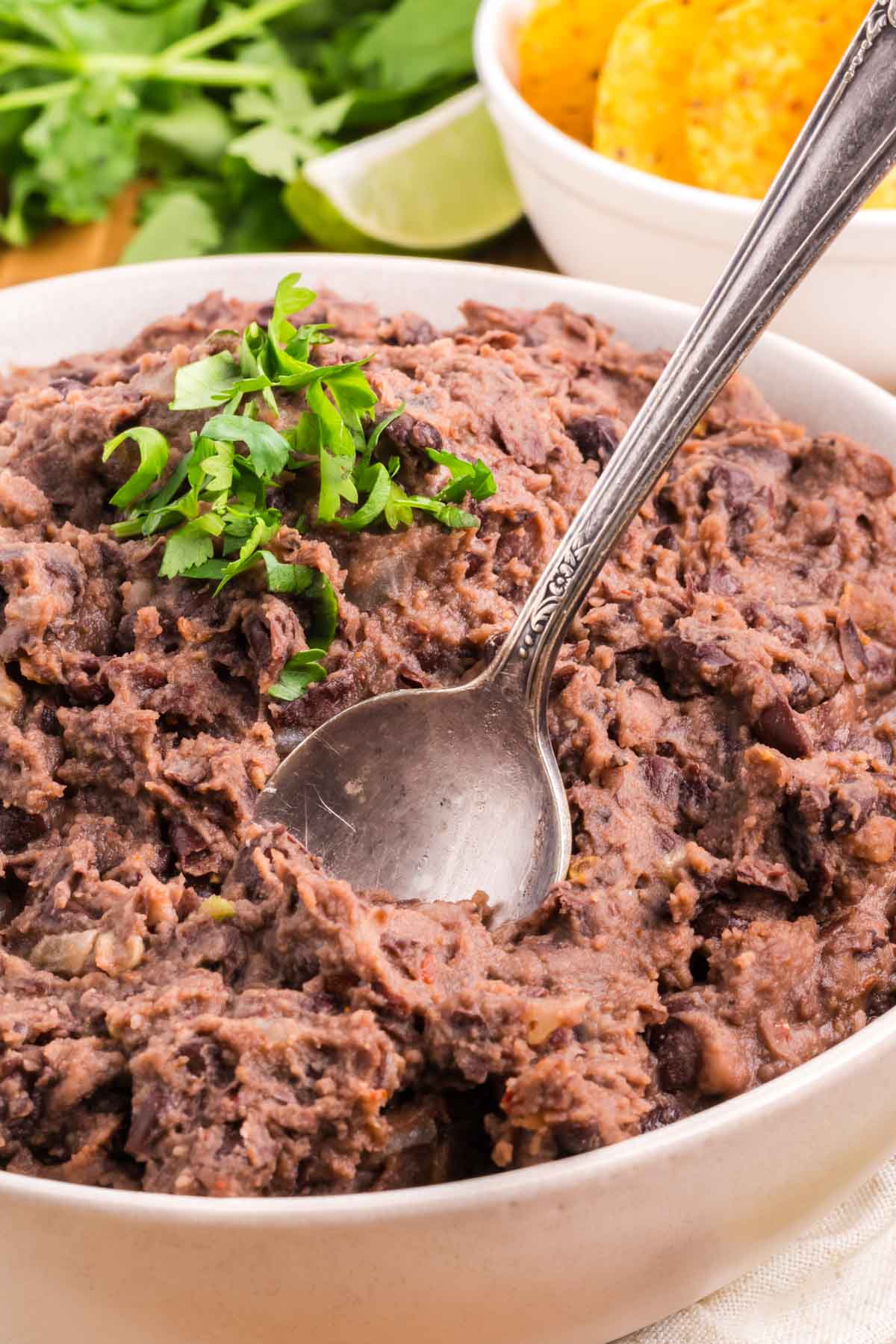 Refried Black Beans in a serving bowl, topped with parsley garnish and a spoon ready to serve.