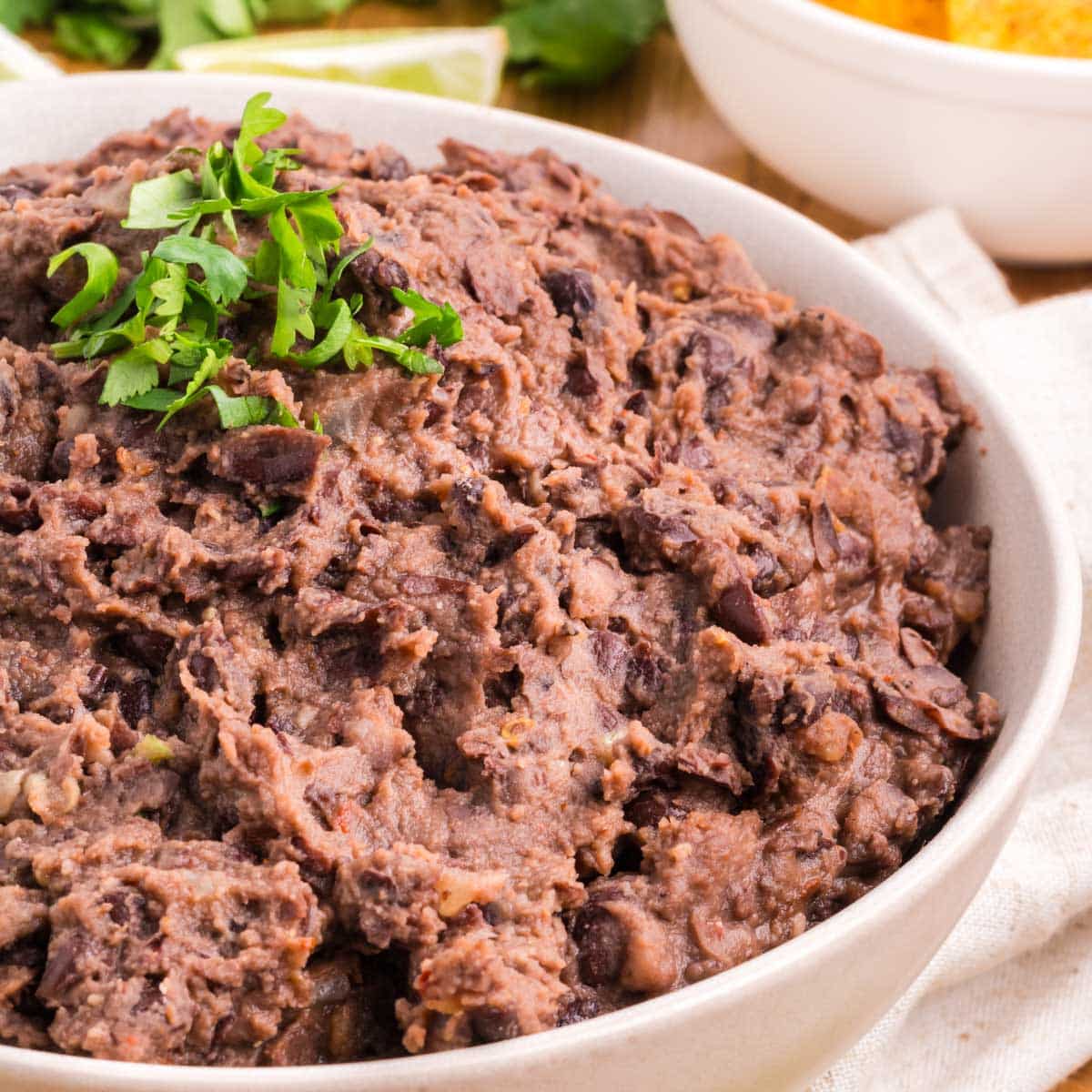 Refried black beans are in a white serving bowl with a green garnish.
