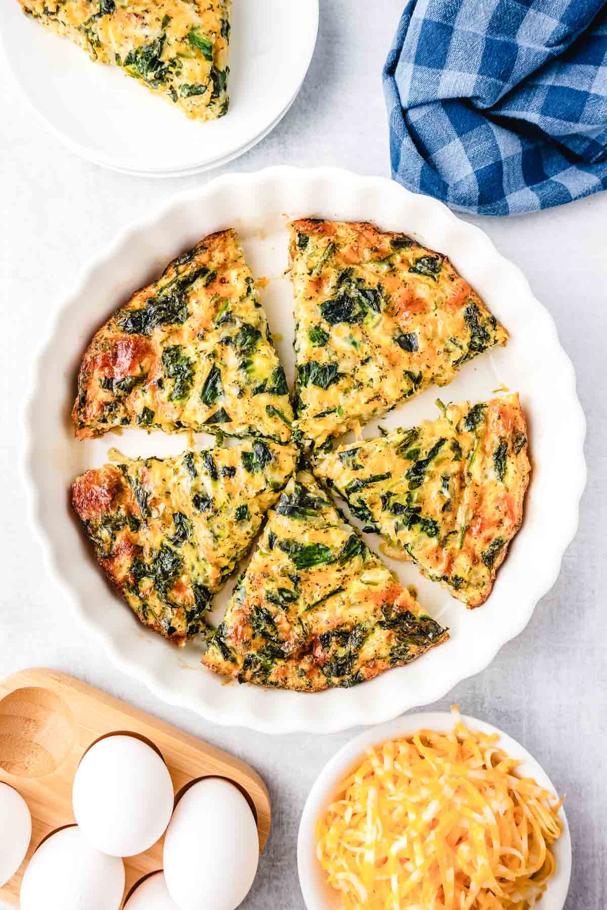 A no crust spinach quiche in a white pie plate cut into slices.