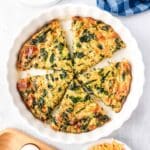 A no crust spinach quiche in a white pie plate cut into slices.