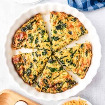 A no crust spinach quiche in a white pie plate cut into slices.