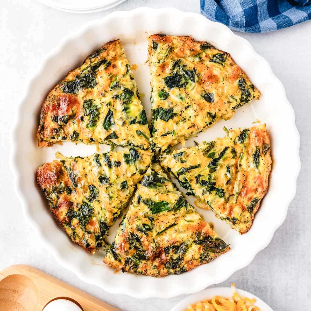 A no crust spinach quiche in a white pie plate cut into slices.