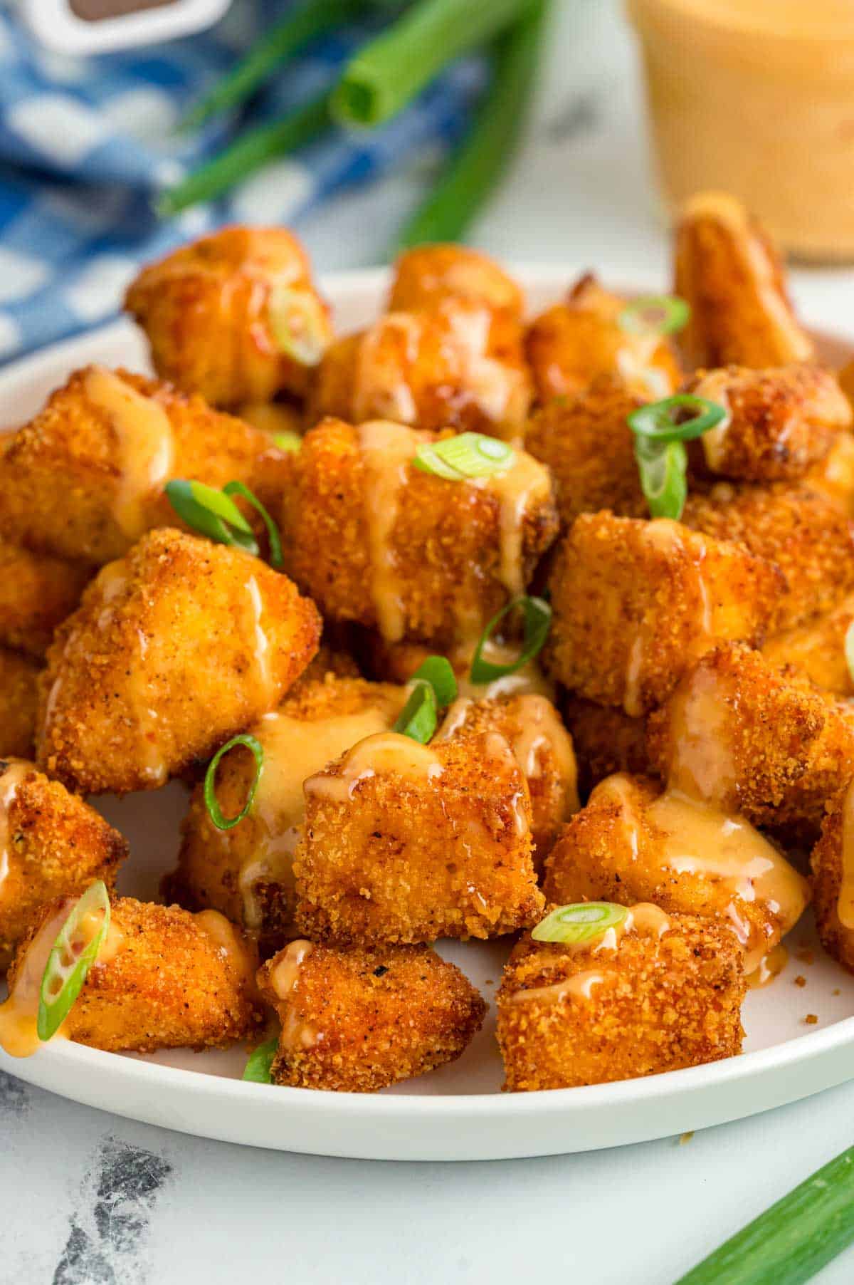 Crispy Salmon Bites on a white plate topped drizzle with bang bang sauce and garnished with sliced green onions.