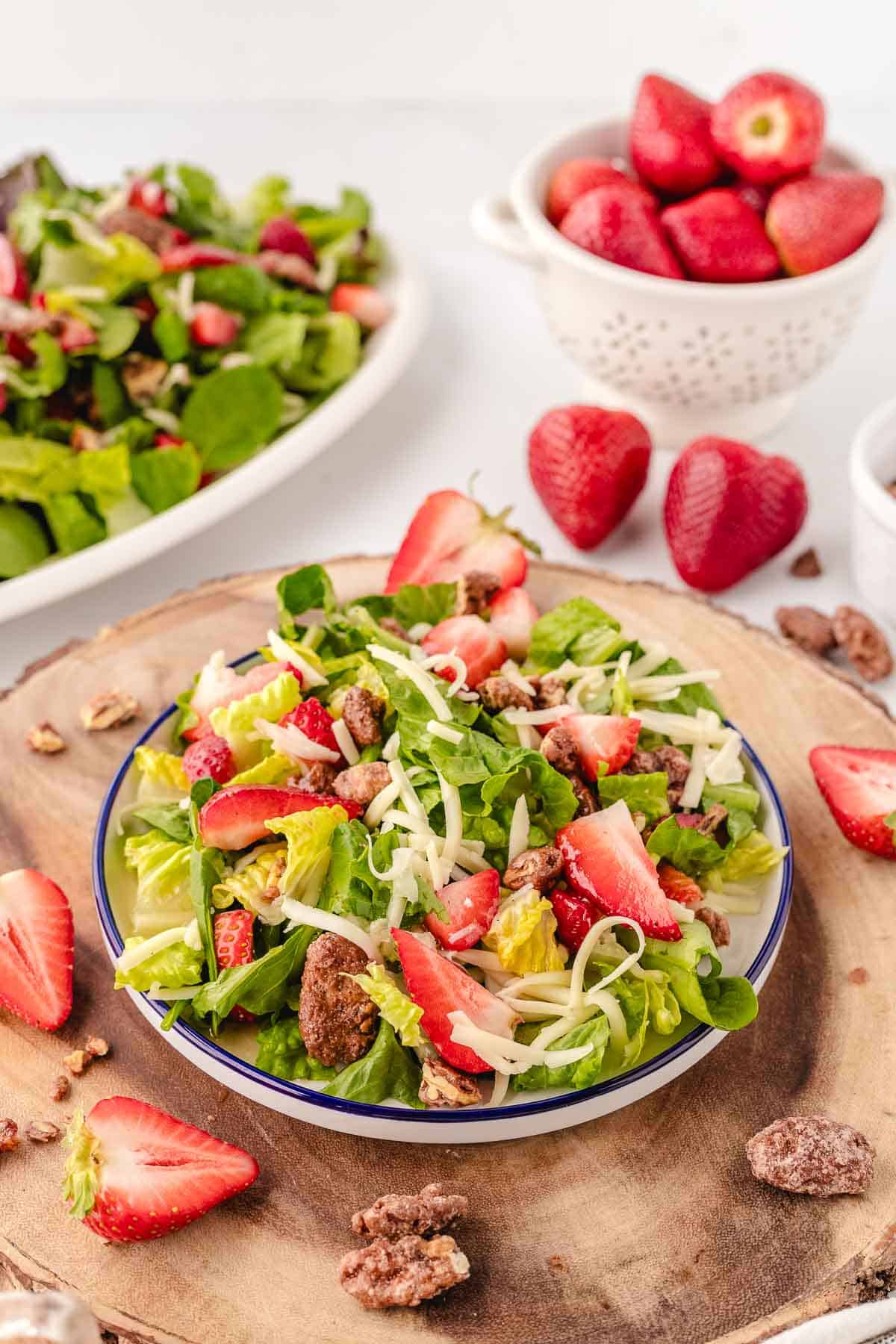 A wooden charger with a white plate with blue rim filled with a praline pecan strawberry salad.