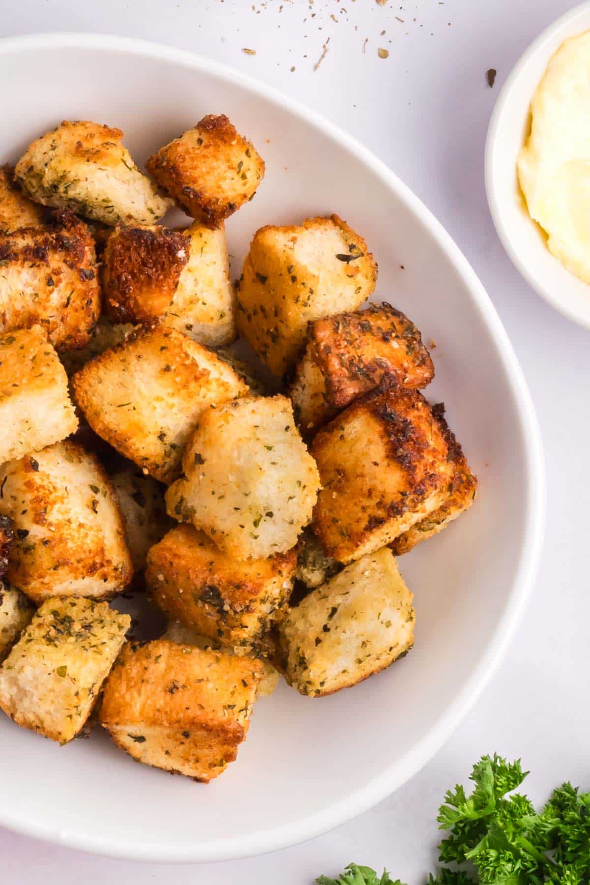 A close up shot of crispy croutons in a white bowl topped with spices.