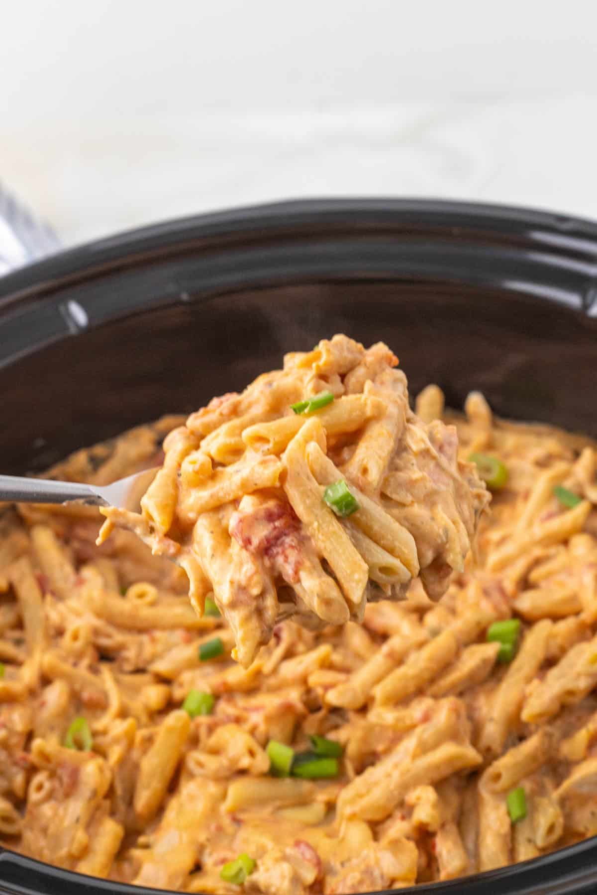 A serving spoon removing pasta from a crockpot.