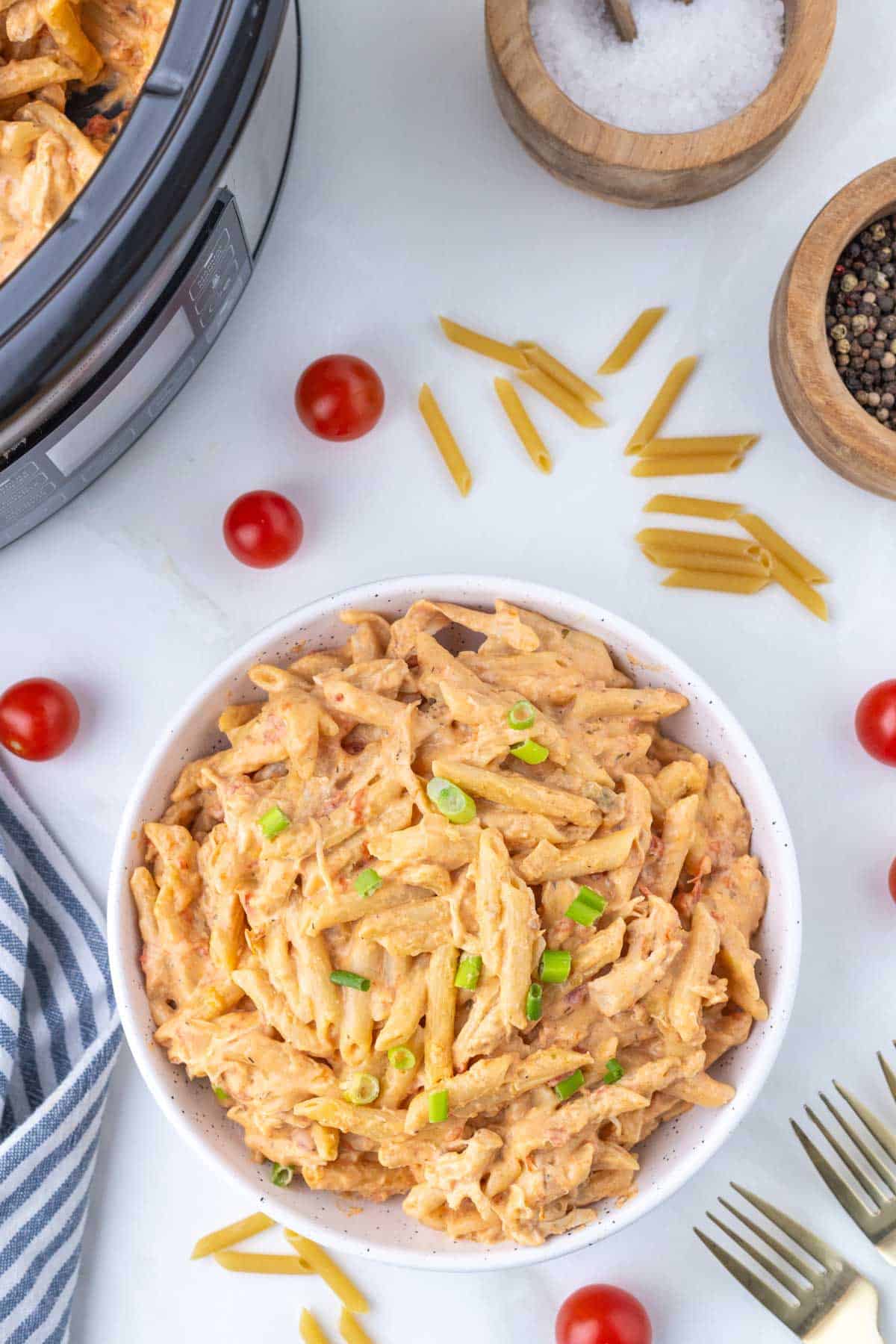 A white bowl of buffalo chicken pasta with a crock pot in the background.