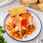 A plate with a serving of pizza pasta bake and a slice of garlic bread.