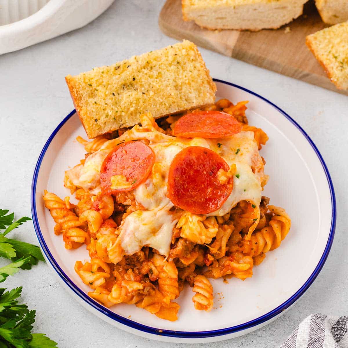 A plate with a serving of pizza pasta bake and a slice of garlic bread.