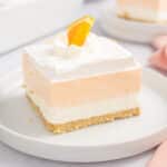 A slice of orange Creamsicle bars on a white plate topped with a slice of orange.