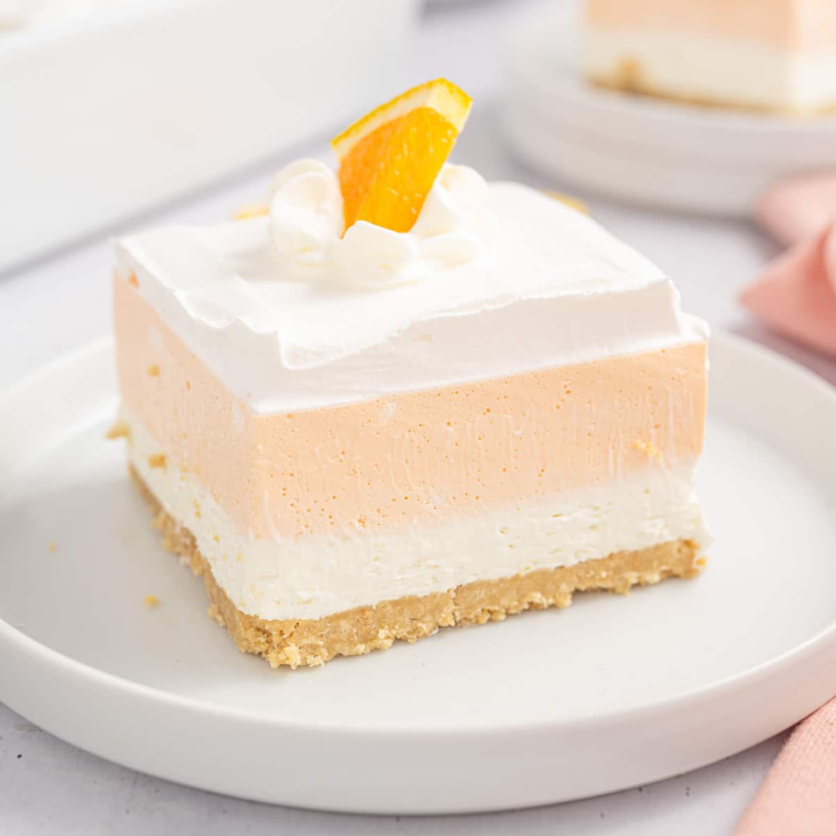 A slice of orange Creamsicle bars on a white plate topped with a slice of orange.