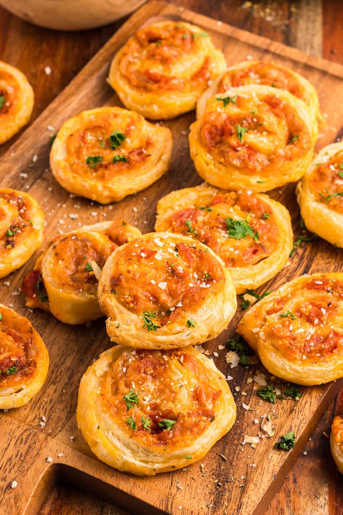 A wooden board tray filled with pepperoni pinwheel appetizers.