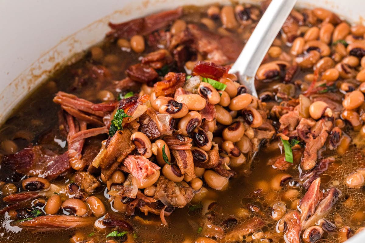 A large serving spoon, removing a scoop of Black Eyed Peas with shredded pieces of ham and bacon.