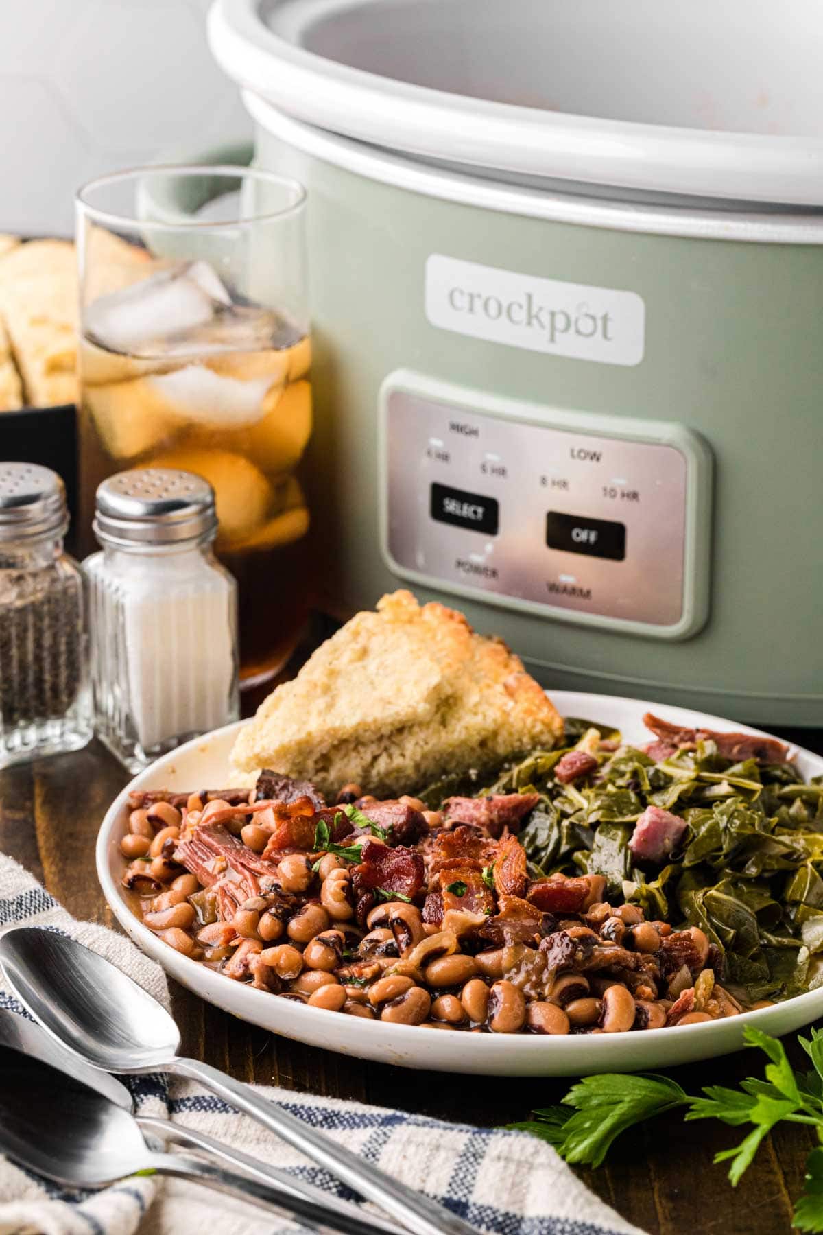 A white plate with Black Eyed Peas, collard greens and cornbread.