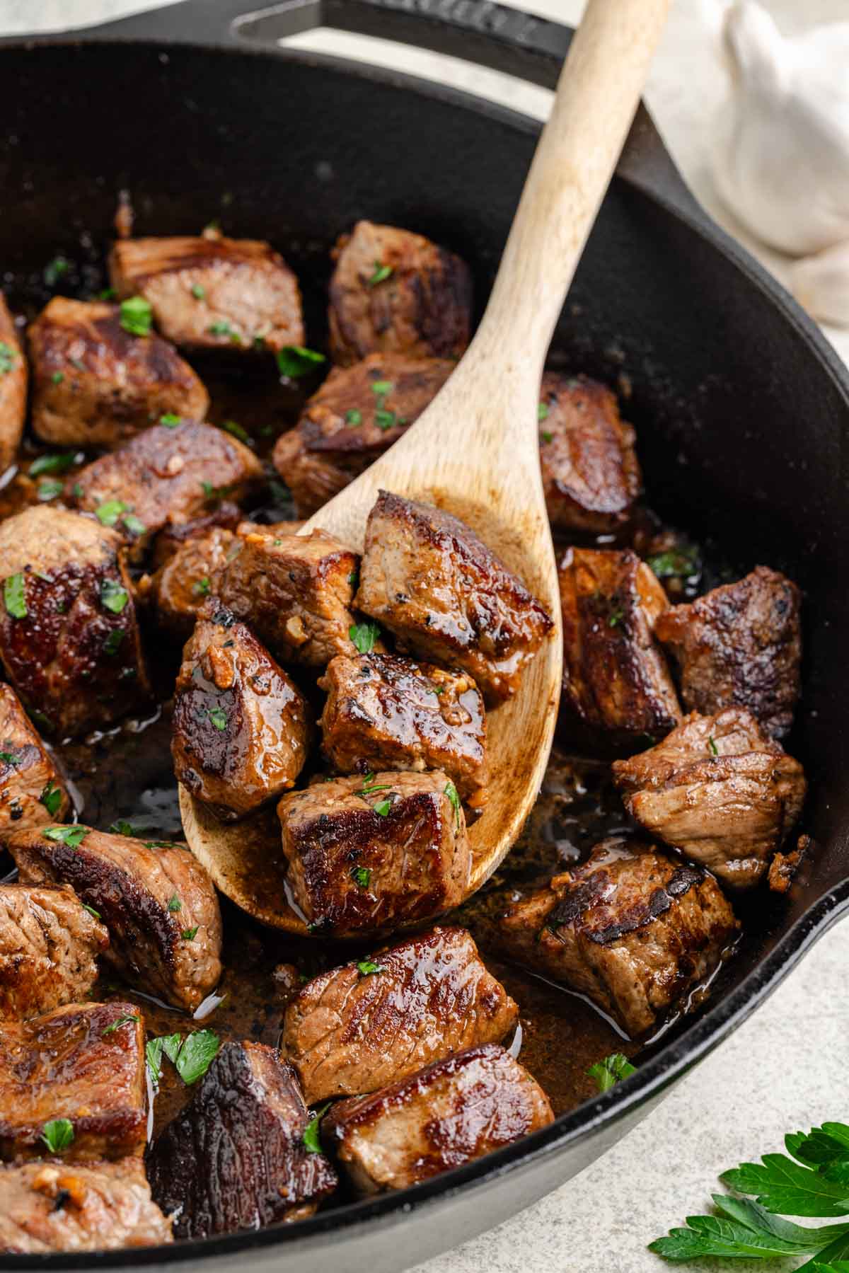A wooden spoon removing a scoop of steak bites.