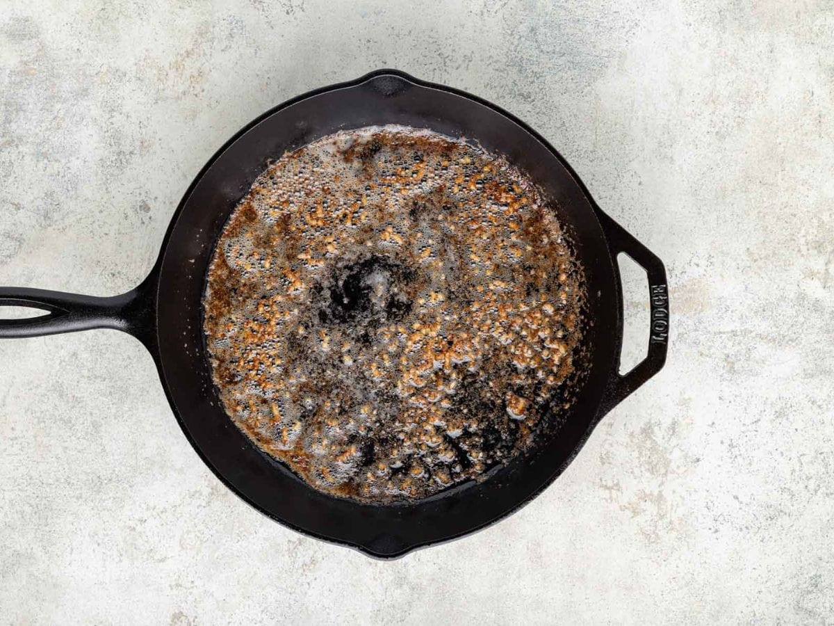 A cast iron skillet with oil. melted butter, and minced garlic.
