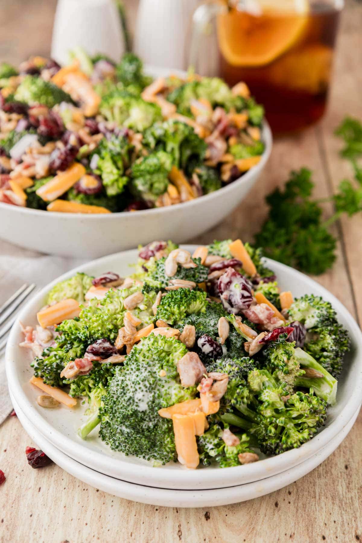 White plate with a portion of broccoli salad with the large bowl of salad in the background.