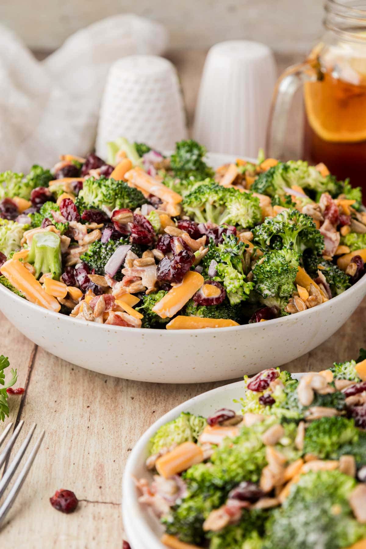 Broccoli salad with bacon in a large bowl next to a plate of salad.