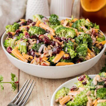Bowl of broccoli salad next to a white plate with a portion of salad on it.