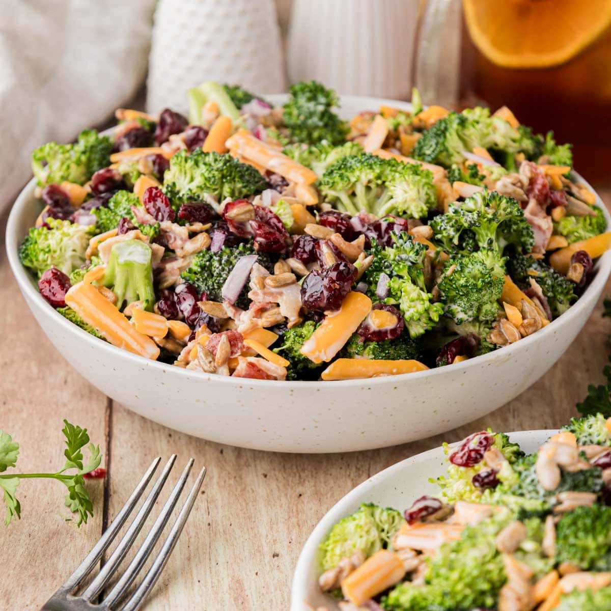 Bowl of broccoli salad next to a white plate with a portion of salad on it.