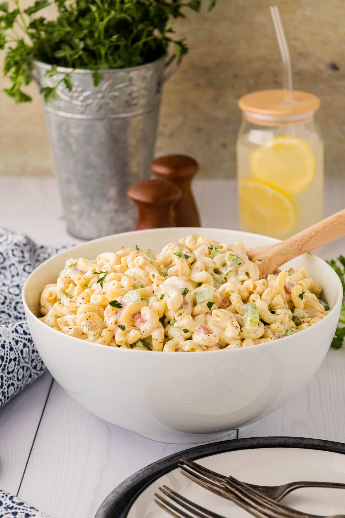 Large white bowl full of macaroni salad with a wooden spoon.