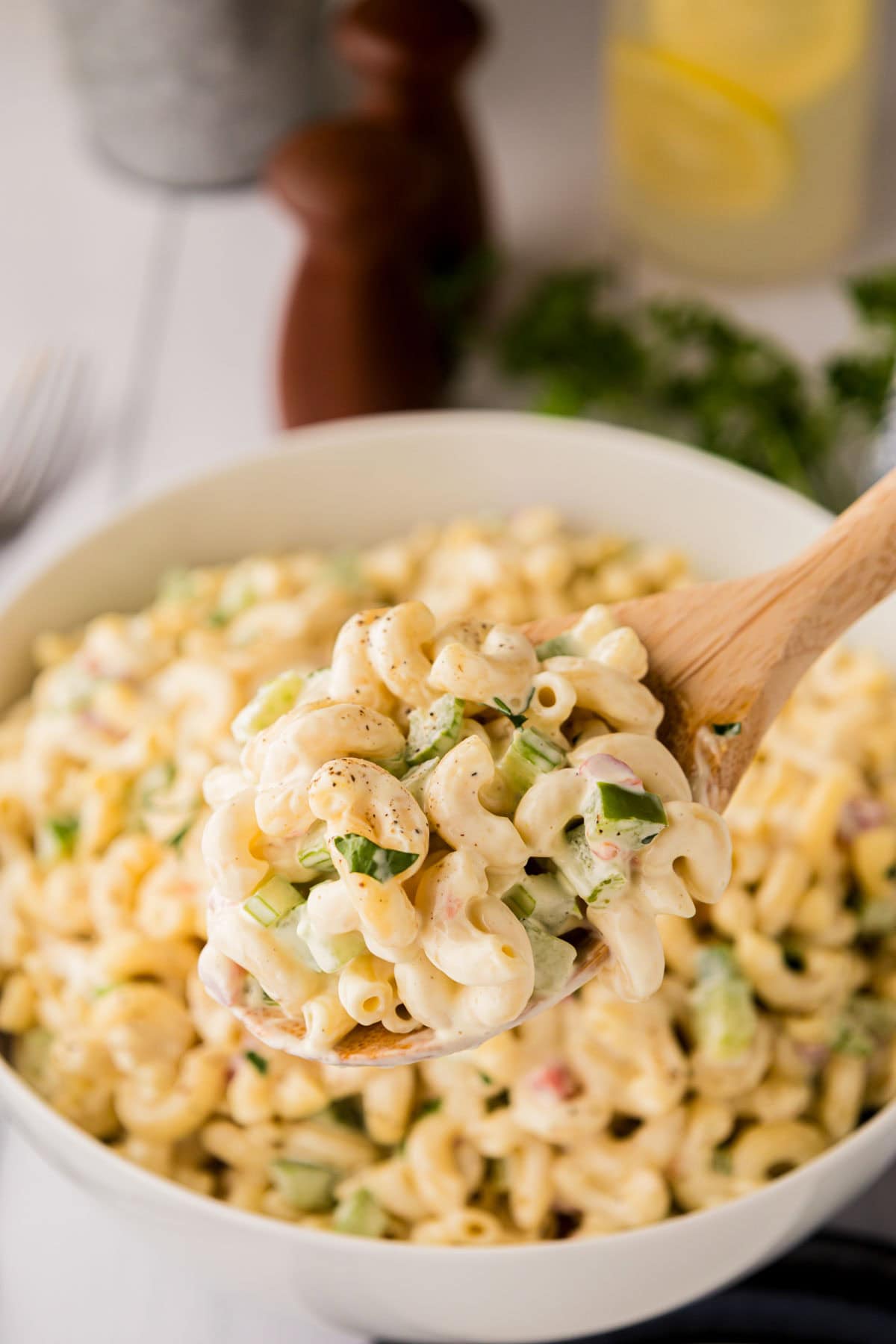 Wooden spoon with a portion of macaroni salad hovering over the bowl of pasta salad.