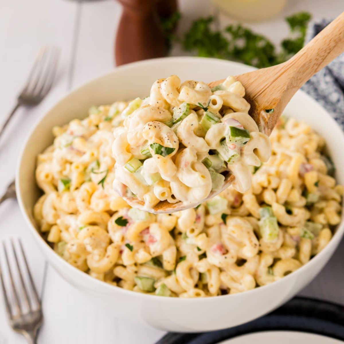 Wooden spoon with macaroni salad on it hovering over the bowl of it.