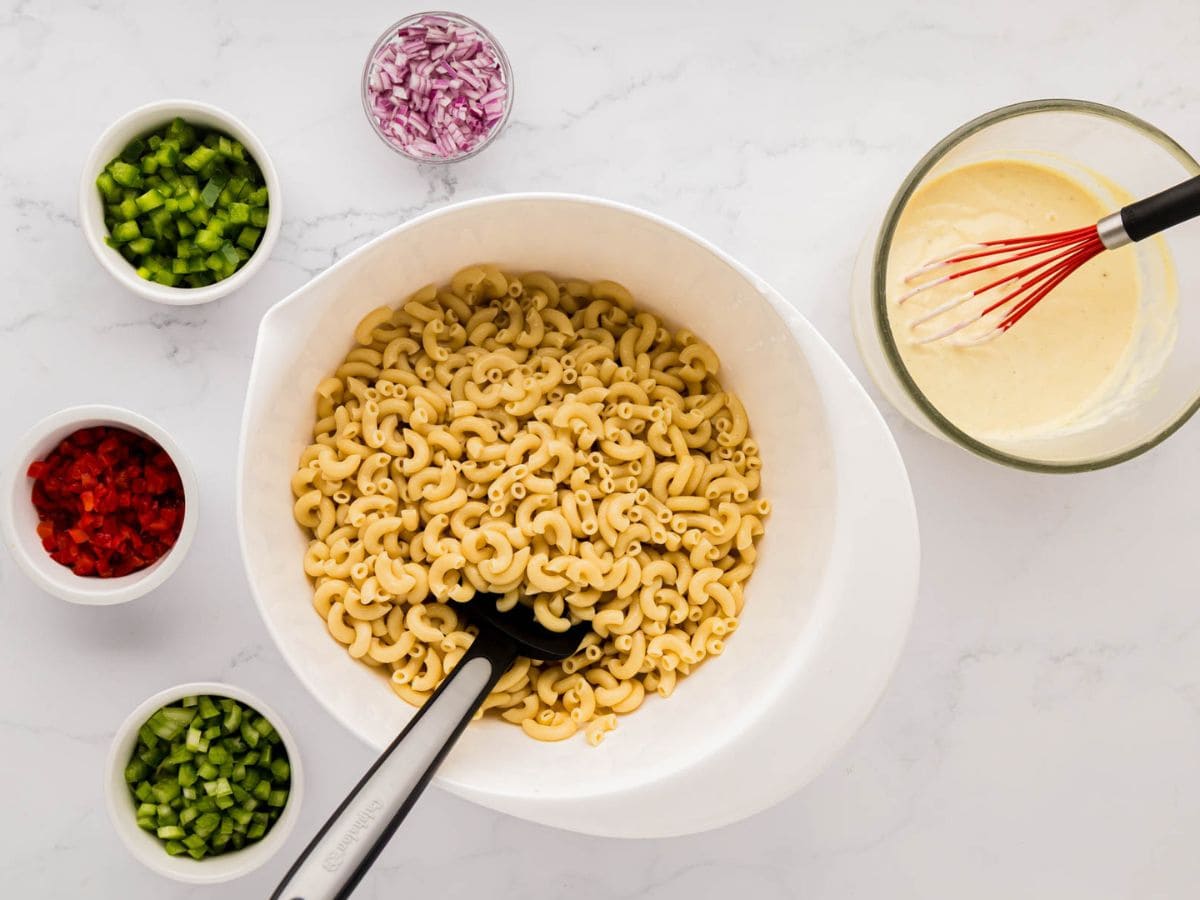 Cooked macaroni in a bowl with the rest of the ingredients for the salad around it.