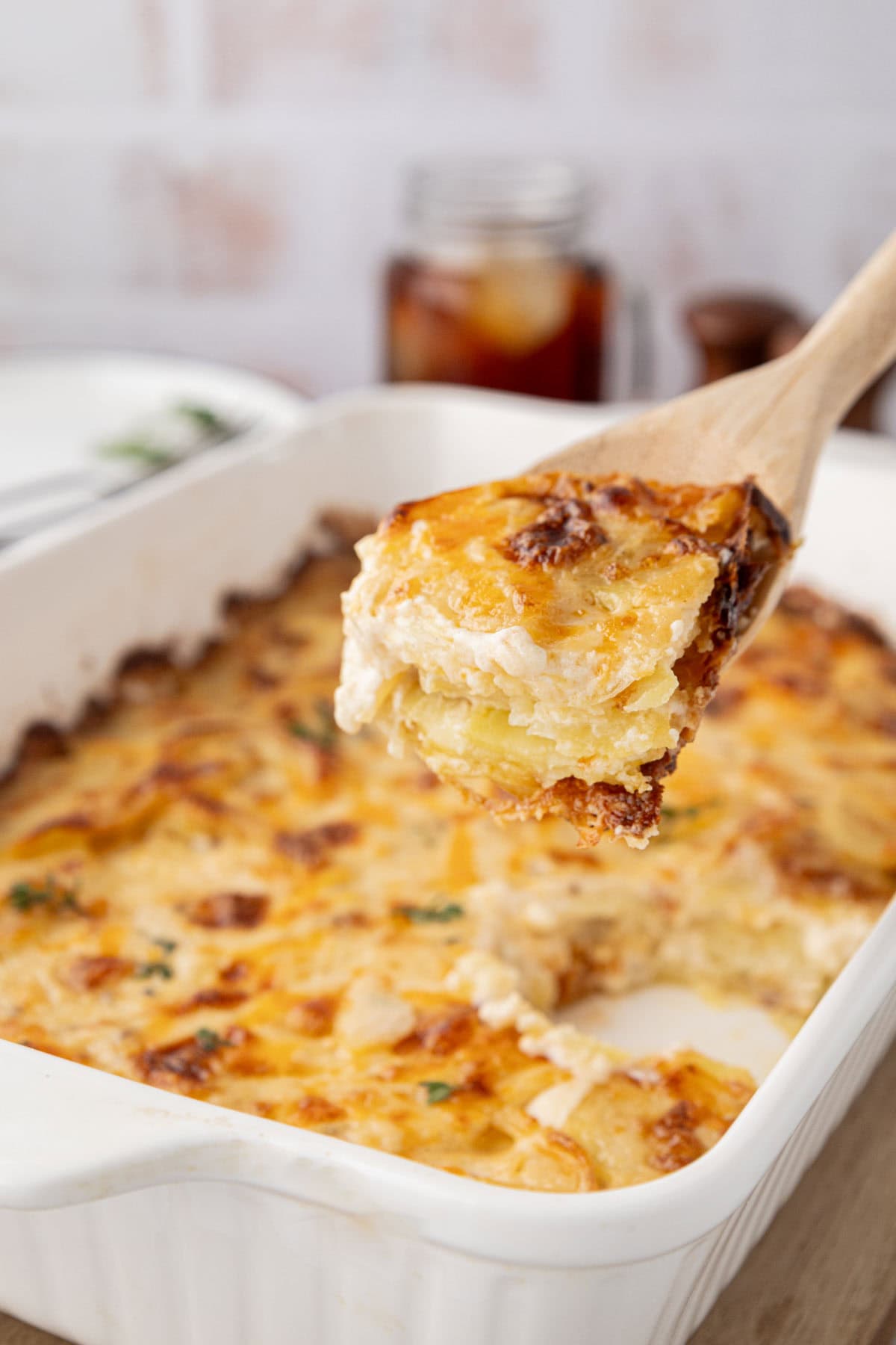 Wooden spoon with a portion of scalloped potatoes from the baking dish.