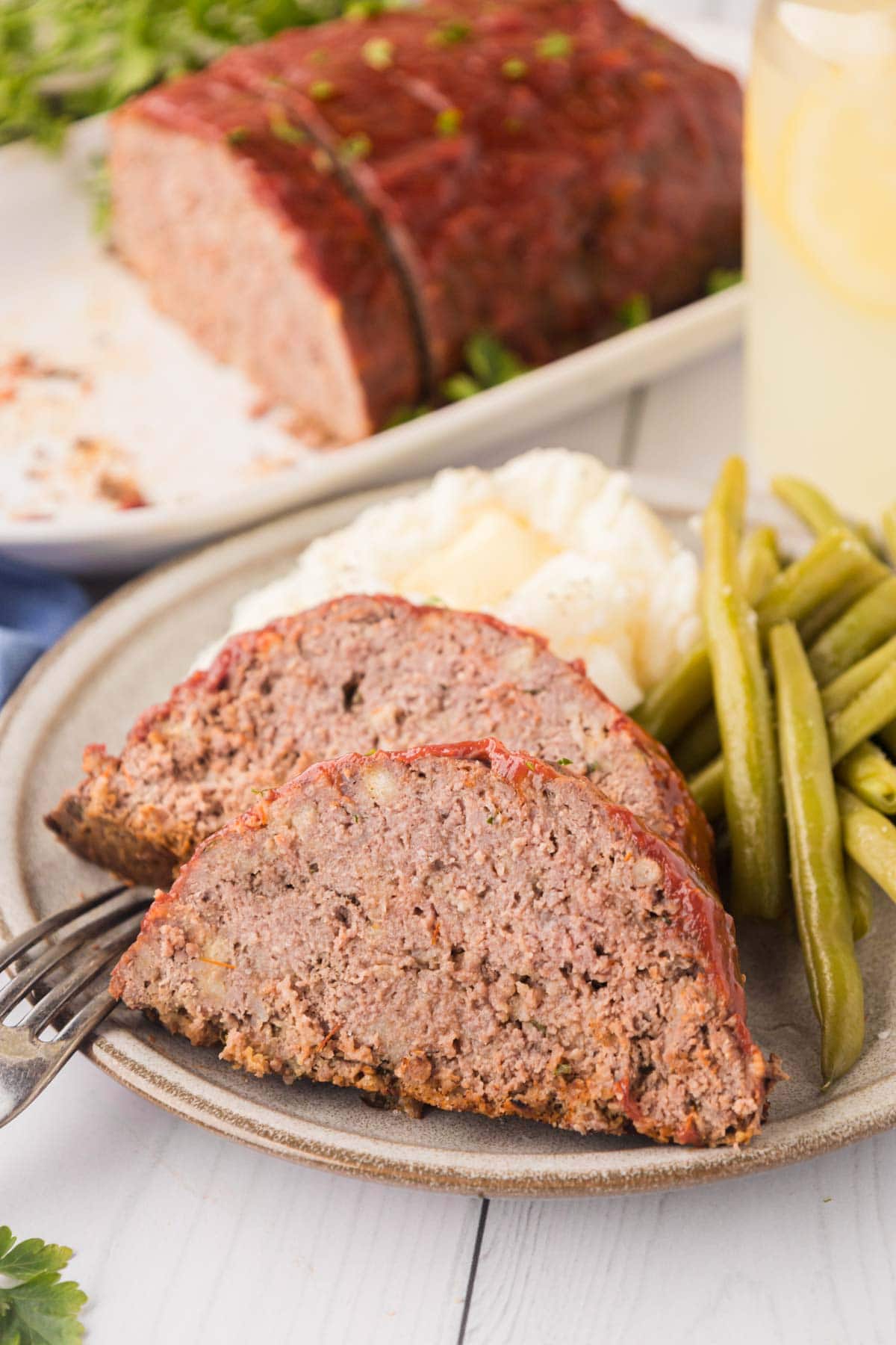 A plate with sliced meatloaf, mashed potatoes, and green beans.