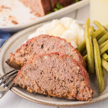 Sliced meatloaf, mashed potatoes, and green beans on a dinner plate.