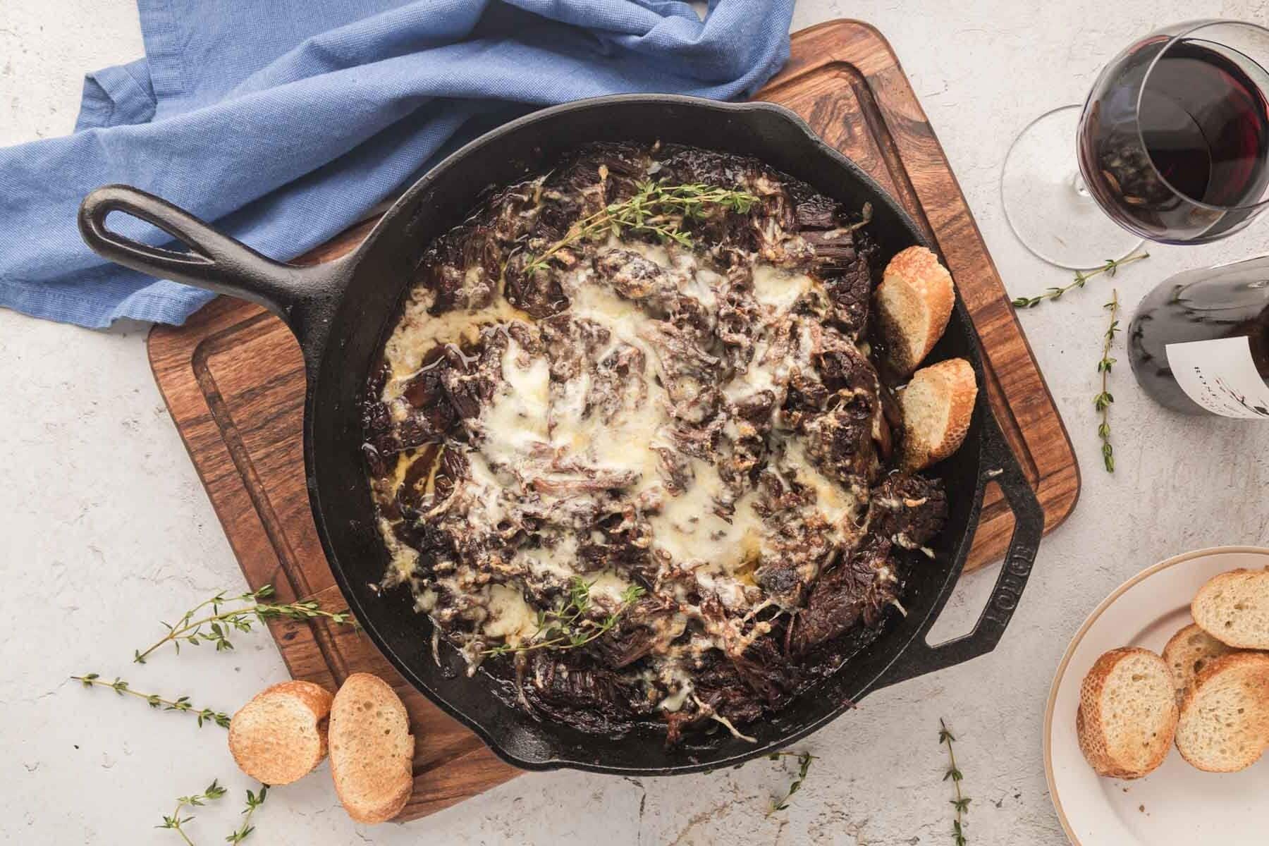 A French onion roast in a cast-iron skillet with pieces of baguette.