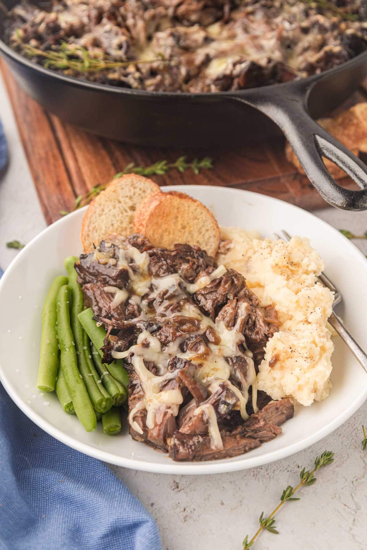 A dinner bowl with green beans, French onion pot roast, and mashed potatoes.