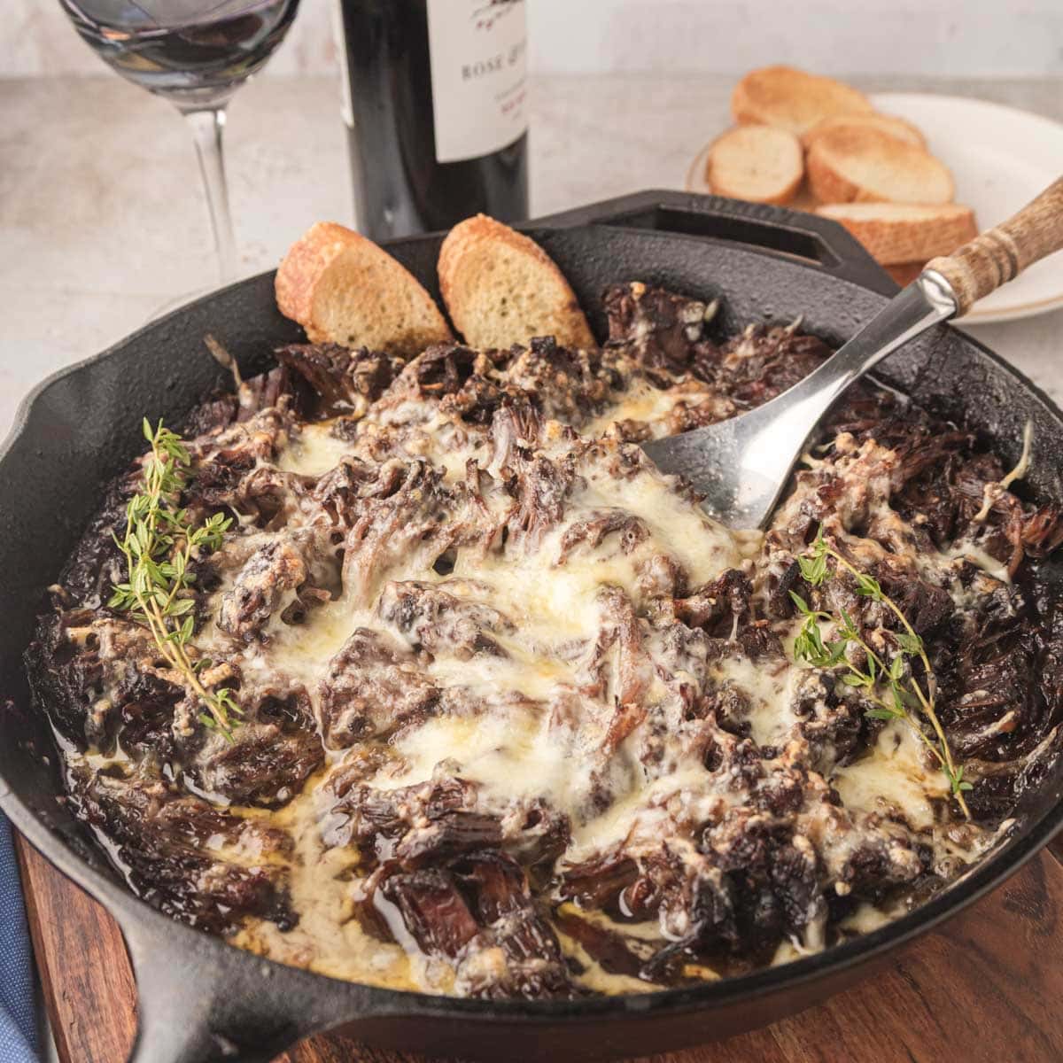 A French onion roast in a cast-iron skillet with pieces of baguette.
