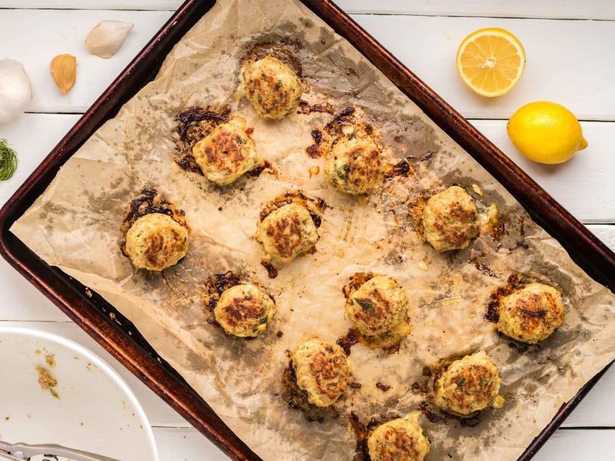 Overhead shot of baked Greek chicken meatballs on a sheet pan.