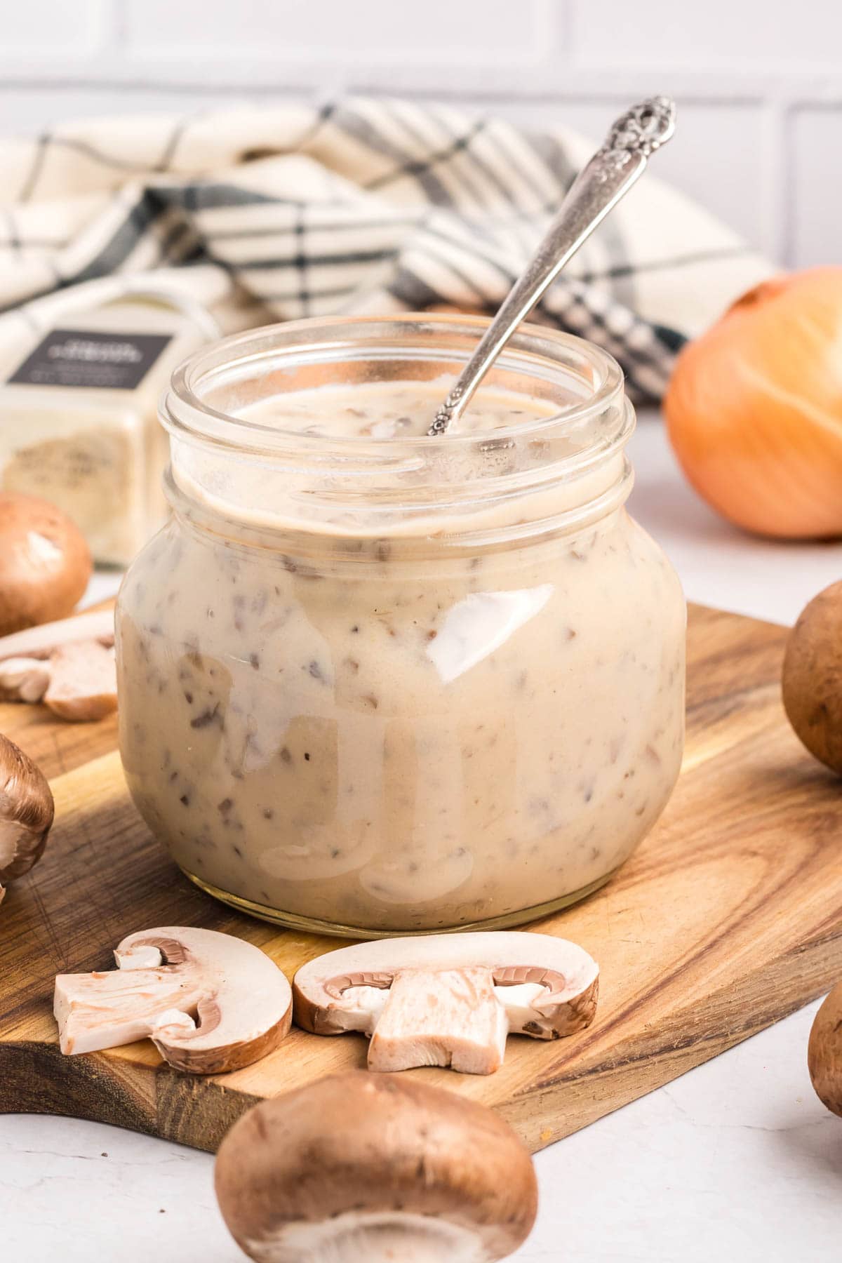 Homemade cream of mushroom soup in a jar with a spoon in it on a wooden board.