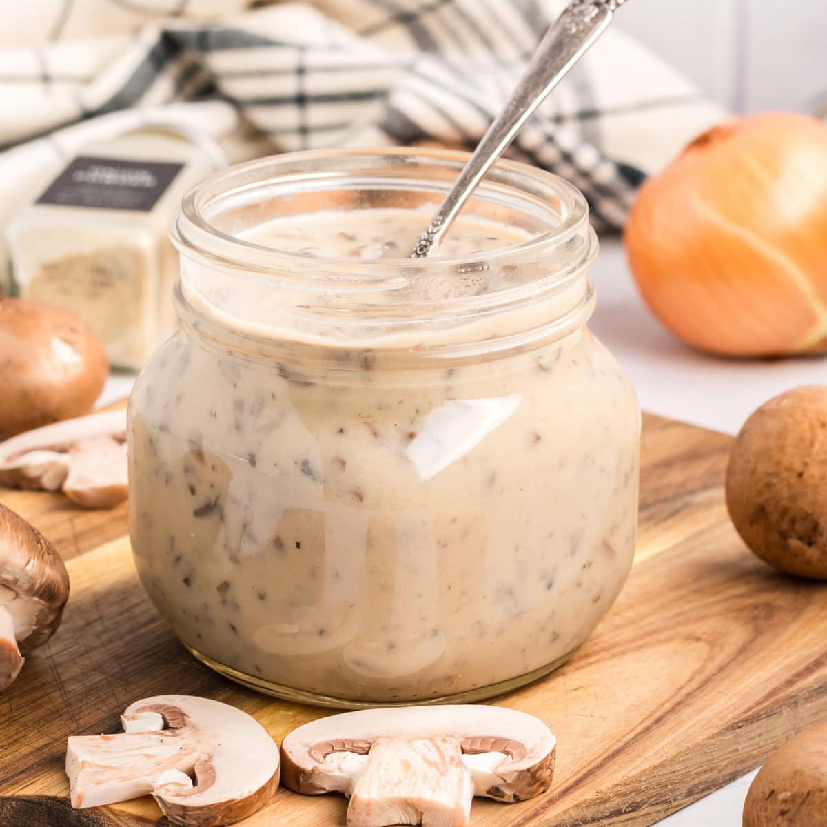 Side view of cream of mushroom soup in a jar on a wooden board with fresh mushrooms around.