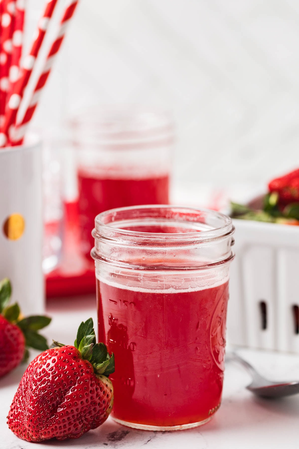 Jar of strawberry syrup next to a fresh strawberry.