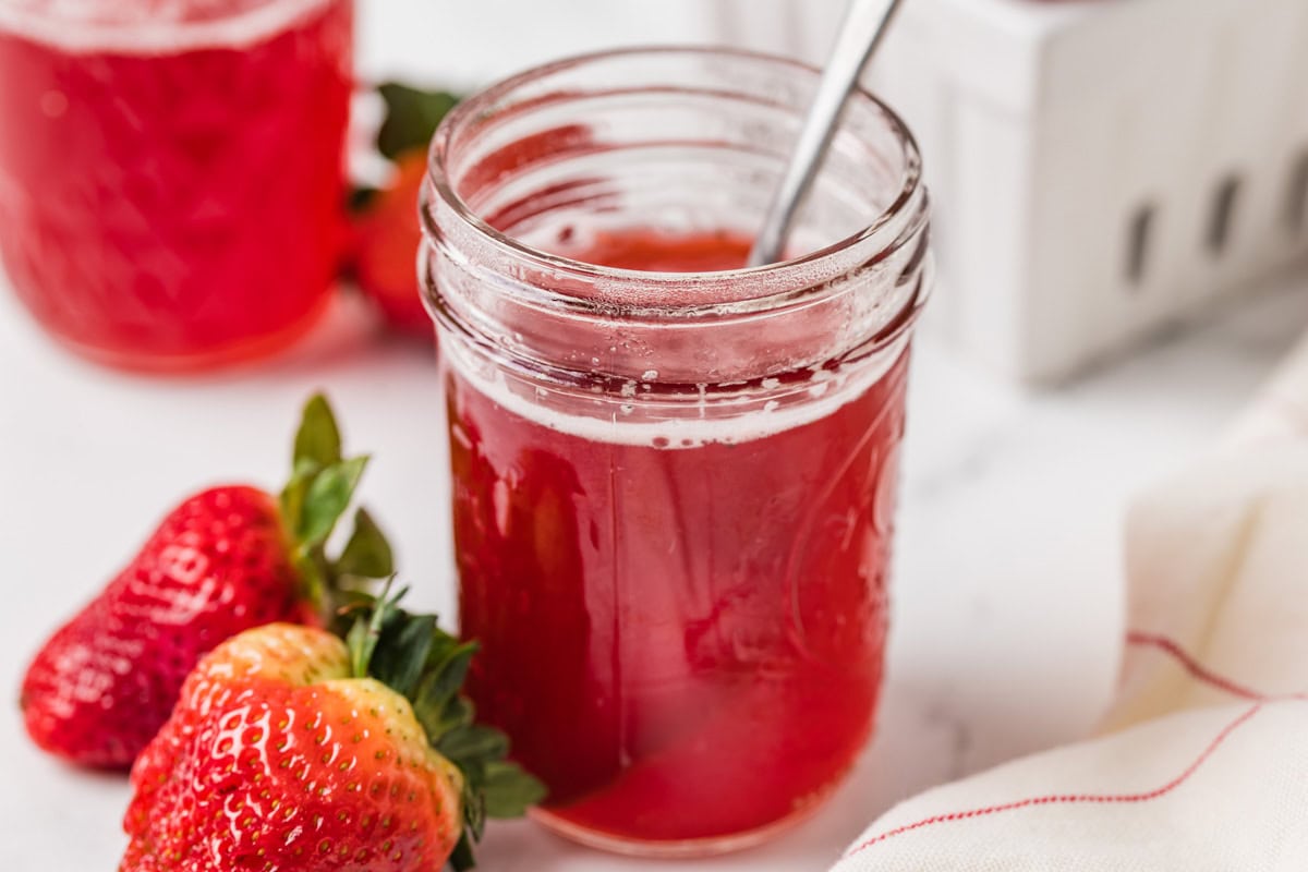 Homemade strawberry syrup in a jar with a spoon.