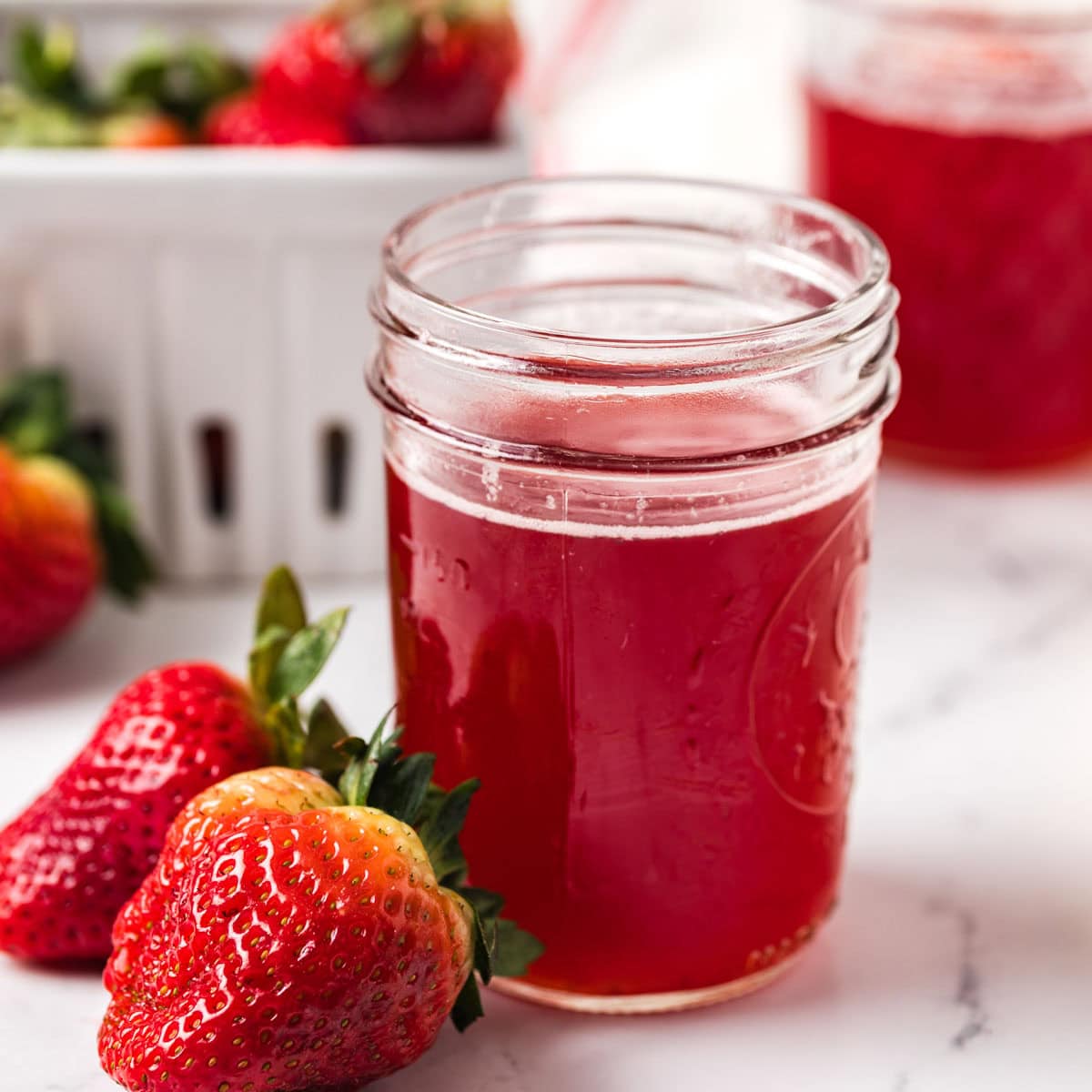Small jar of homemade strawberry syrup next to two fresh strawberries.