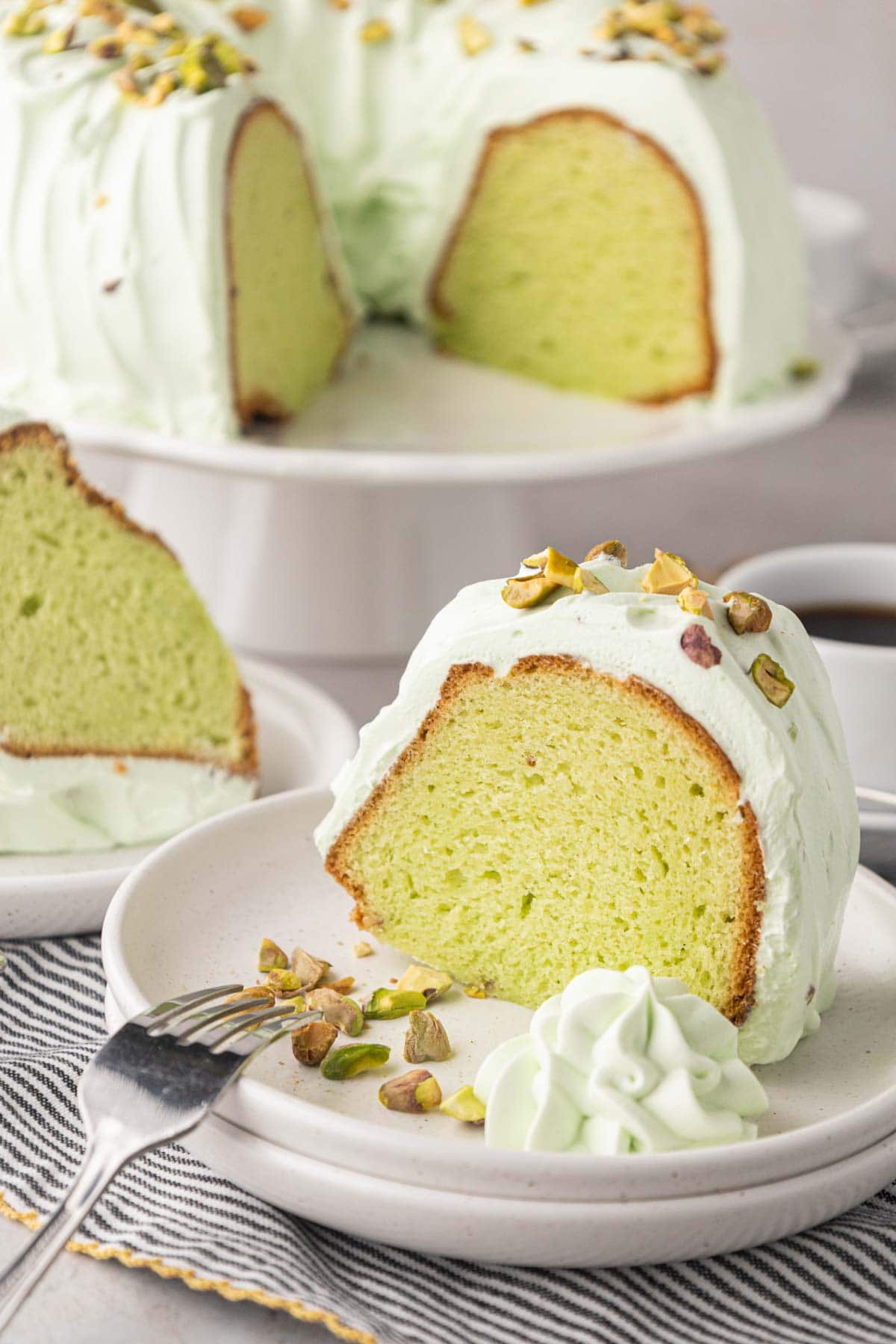 A slice of pistachio cake on a white plate with whipped pistachio icing.