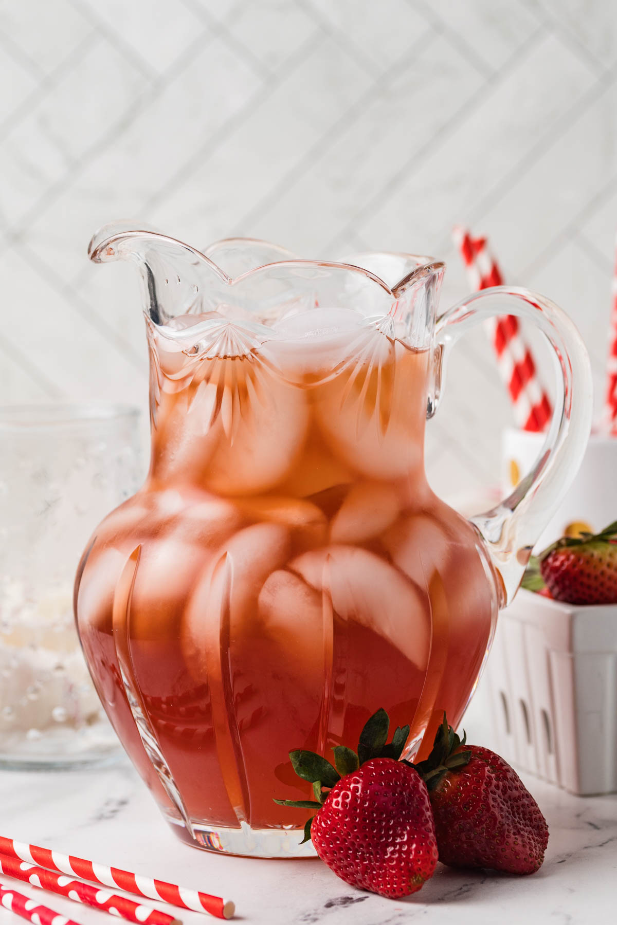 Pitcher of Strawberry iced tea next to fresh strawberries on a counter.