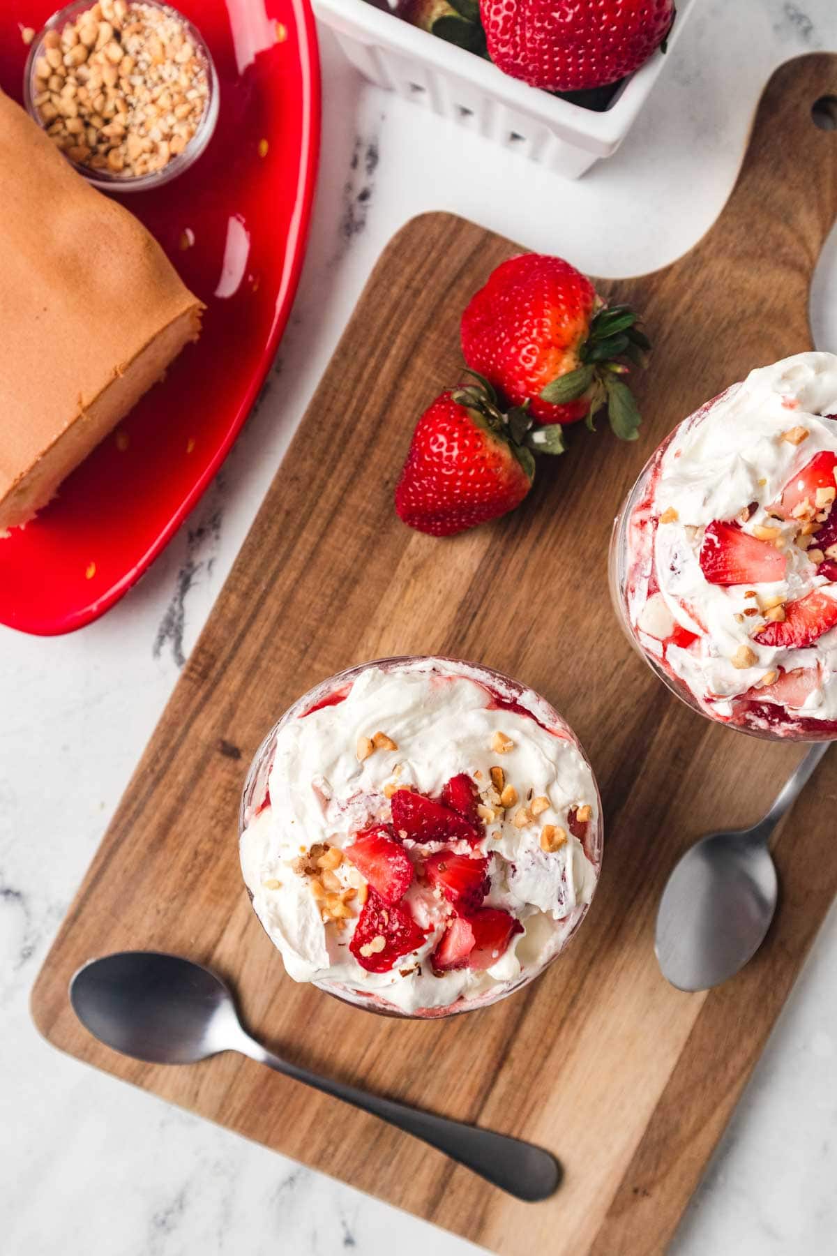 Overhead shot of two strawberry shortcake ice cream sundaes on a wooden board.