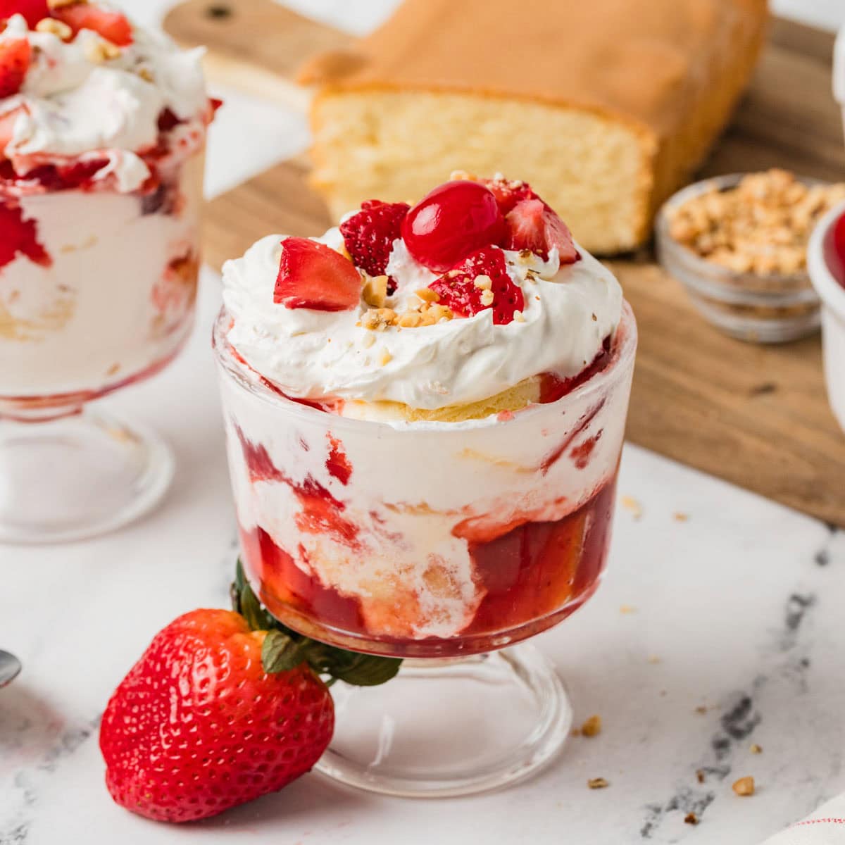 Strawberry shortcake ice cream sundae in a small glass next to a fresh strawberry.