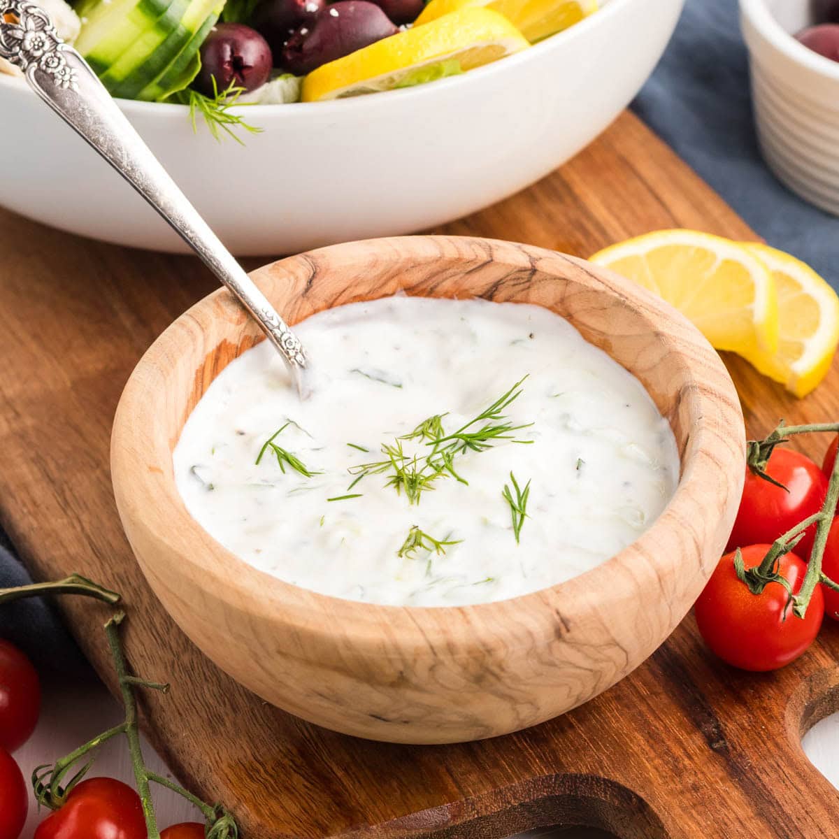 Homemade tzatziki sauce in a wooden bowl with fresh dill on top.