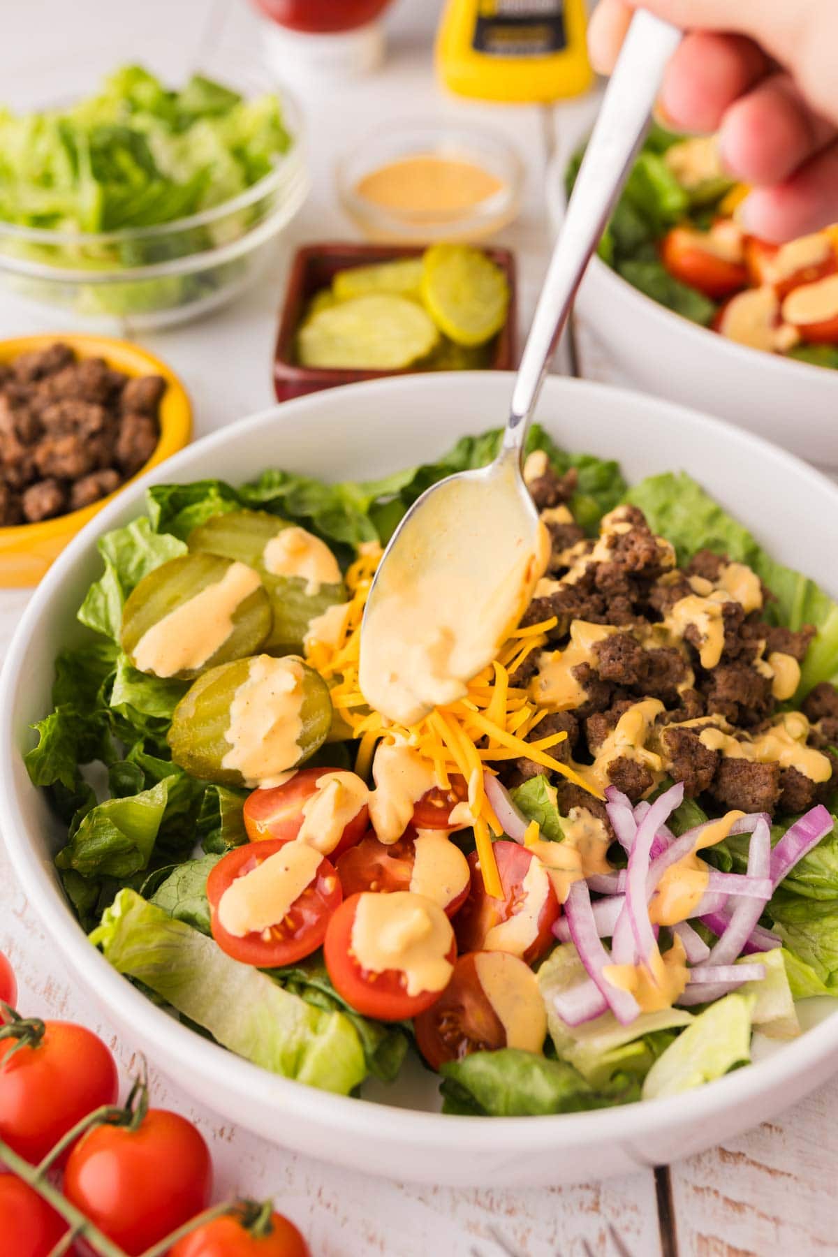 Hand drizzling the big mac salad dressing on the salad in a white bowl.