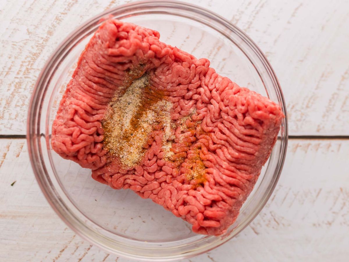Ground beef in a bowl with seasoning on top.
